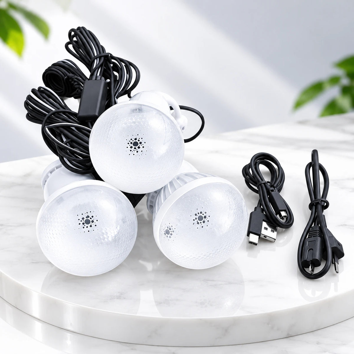 Three white LED light bulbs with black cords and a USB charging cable, arranged on a white marble tray with a soft-focus indoor background.