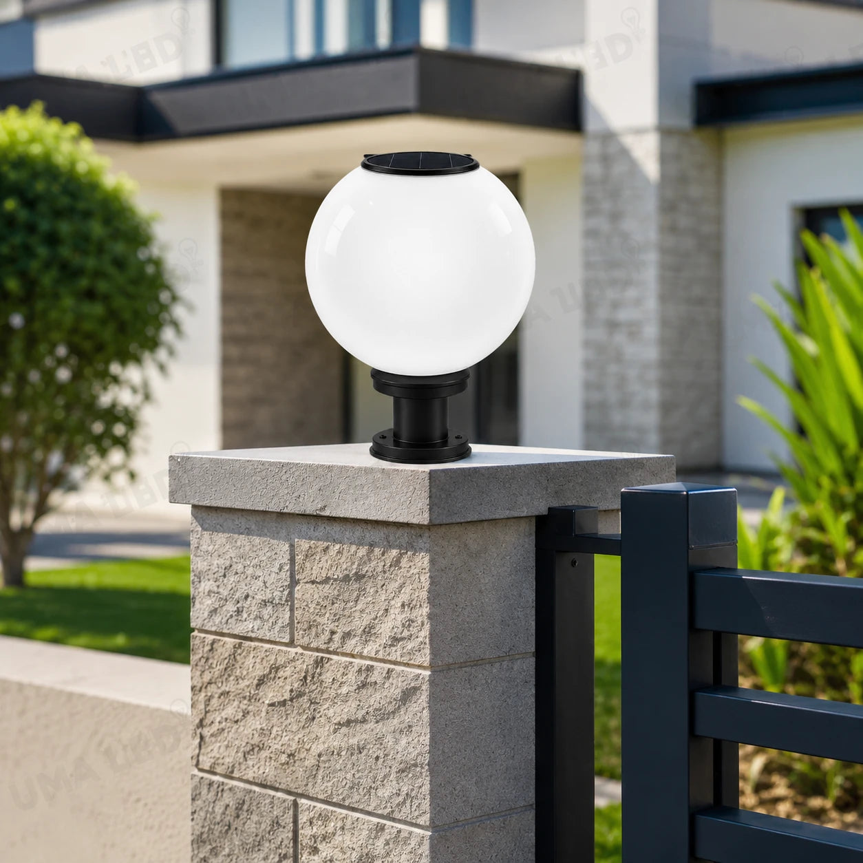 A modern solar-powered outdoor globe light with a white spherical shade and black base, mounted on a stone pillar next to a dark metal gate in front of a house.