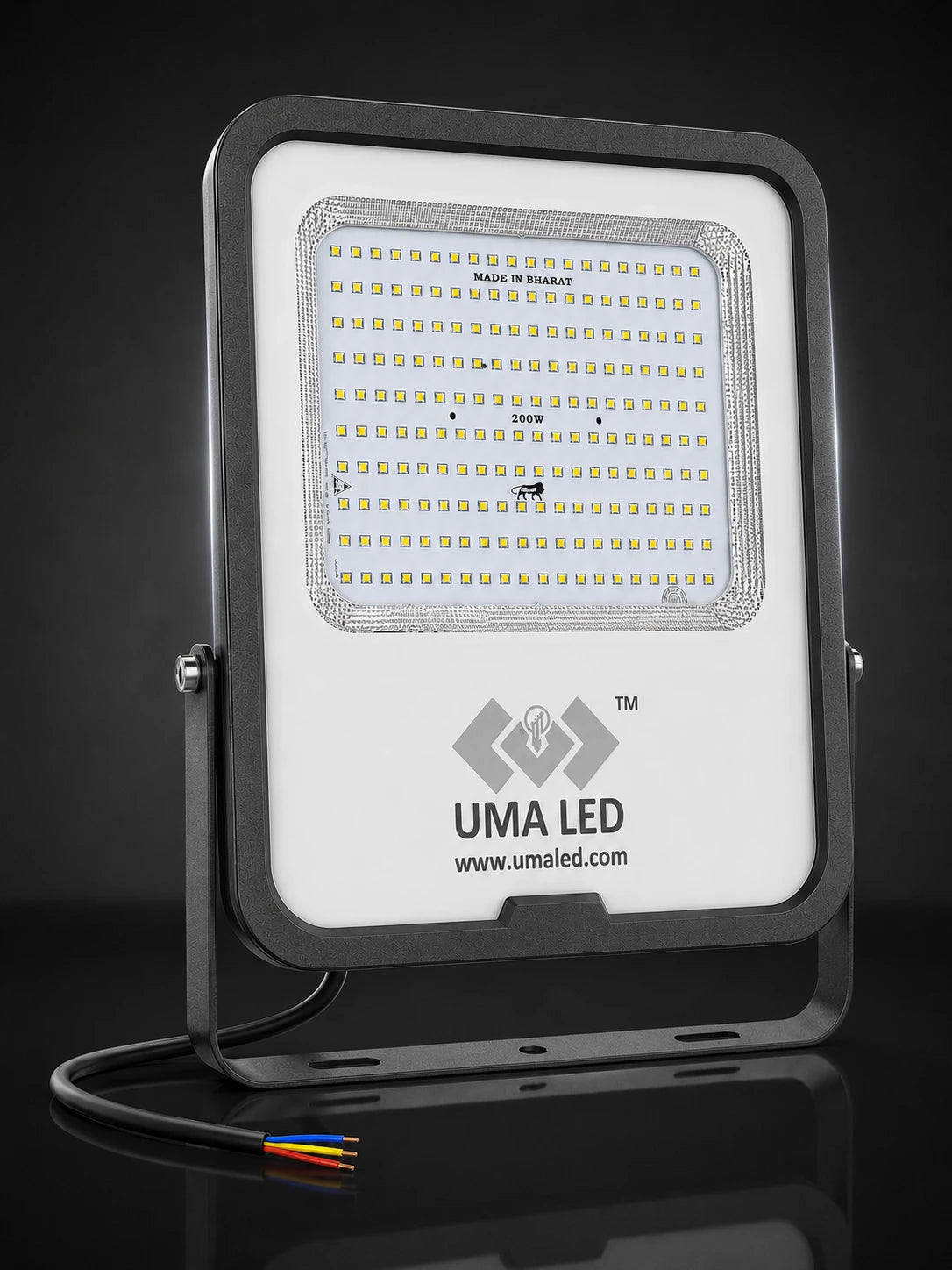 UMA LED square floodlight with a white faceplate, black housing, and visible internal LED array, shown on a dark reflective studio background with a cable and small multicolored wire visible at the bottom.