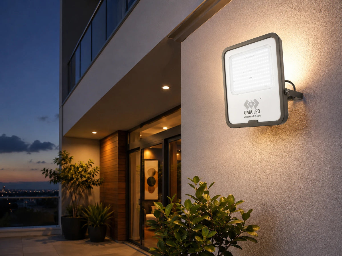 A wall-mounted UMA LED outdoor light fixture glowing warm white on the beige stucco wall of a modern building at dusk.