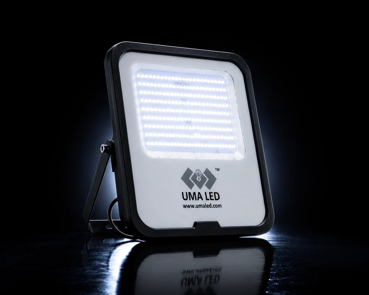 UMA LED square floodlight with a black frame and white LED panel, shown illuminated on a reflective black surface against a dark background.