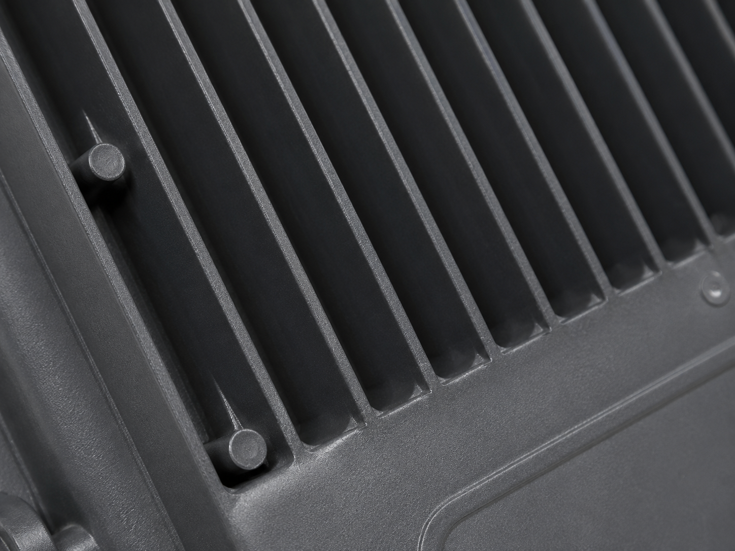 Close-up of a dark gray ribbed metal surface with a slotted vent design and small fasteners.