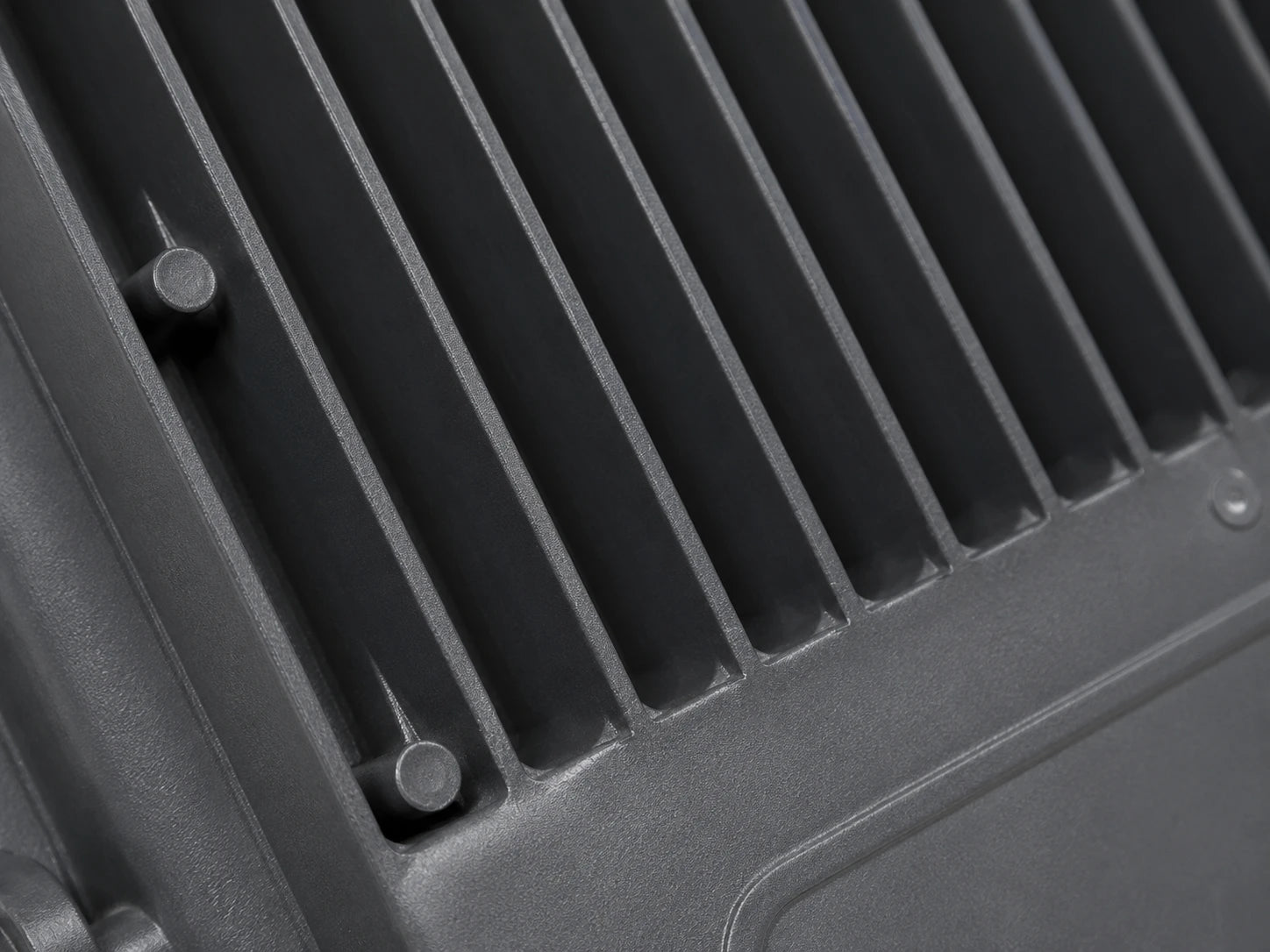 Close-up of a dark gray ribbed metal surface with a slotted vent design and small fasteners.
