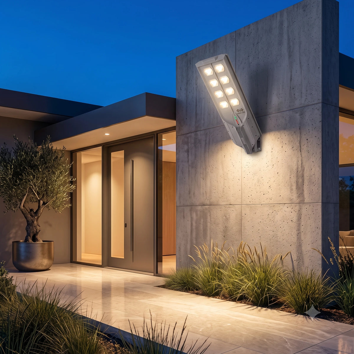 Modern outdoor wall sconce light fixture mounted on a concrete house exterior at dusk, casting warm light onto a tiled walkway and landscaped plants.